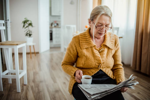 istock An elderly woman reading a newspaper at home and drinking coffee 1214915059
