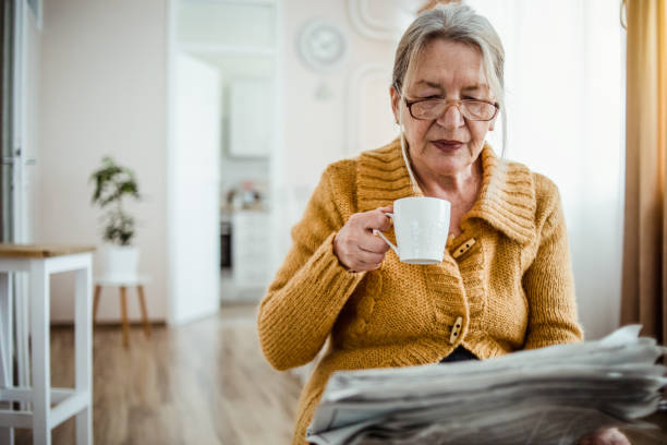 istock An elderly woman reading a newspaper at home and drinking coffee 1214915077