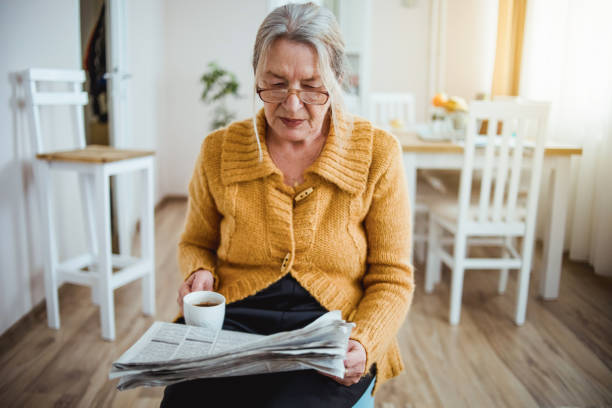 istock An elderly woman reading a newspaper at home and drinking coffee 1214915469
