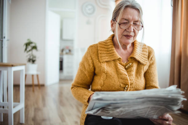 istock An elderly woman reading a newspaper at home and drinking coffee 1214915472