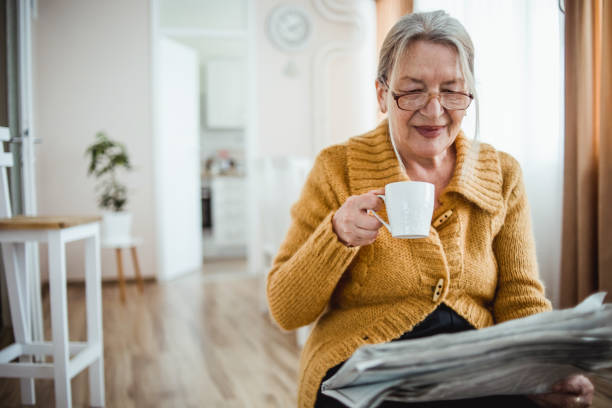 istock An elderly woman reading a newspaper at home and drinking coffee 1214915903
