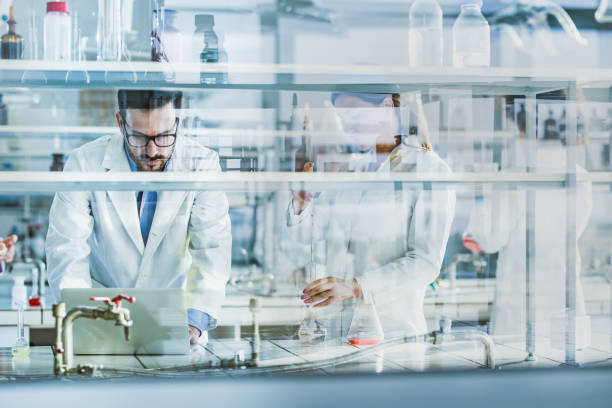 Group of biochemists working on new virus research in laboratory. Team of scientists working on scientific research in laboratory. The view is through glass. science research stock pictures, royalty-free photos & images