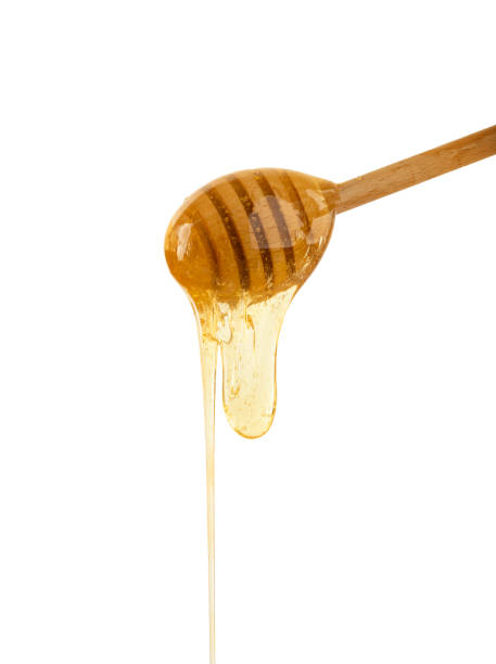 istock Close up honey flowing from wooden dipper on white 1214920379