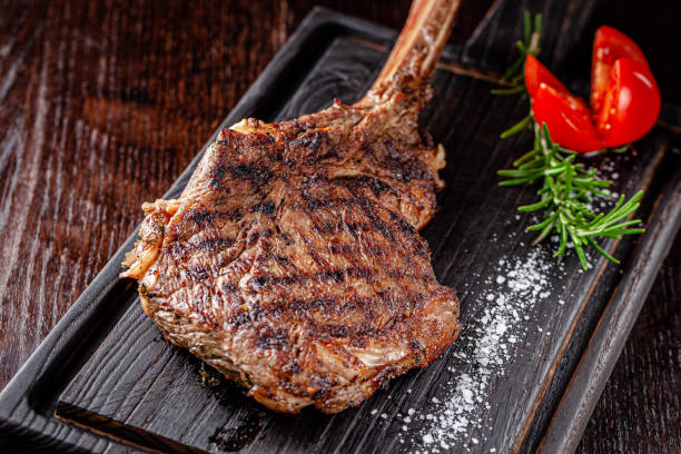 American cuisine. Large juicy grilled steak on a tomahawk bone. Beef steak on a wooden board with rosemary and salt. background image, copy space text American cuisine. Large juicy grilled steak on a tomahawk bone. Beef steak on a wooden board with rosemary and salt. background image, copy space text blade roast stock pictures, royalty-free photos & images