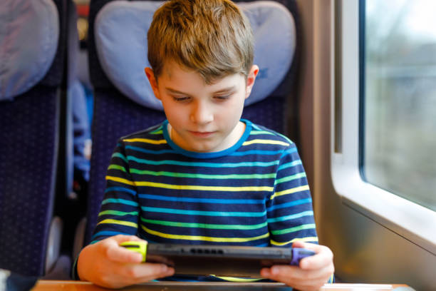 istock Cute adorable kid boy playing electronic games on tablet gadget during traveling by train. Happy child sitting near window. Family going on vacations 1214924282