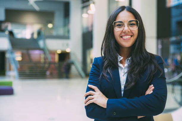 Happy successful businesswoman posing in office hall Happy successful businesswoman posing in office hall. Young Latin woman wearing formal suit and glasses, standing for camera with arms folded, smiling. Business portrait concept latin woman stock pictures, royalty-free photos & images