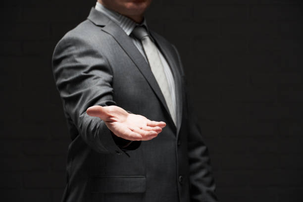 ritratto uomo d'affari che mostra palmo di mano, per dimostrare qualcosa, vestito in abito grigio, sfondo parete scura - suit necktie close up gray foto e immagini stock