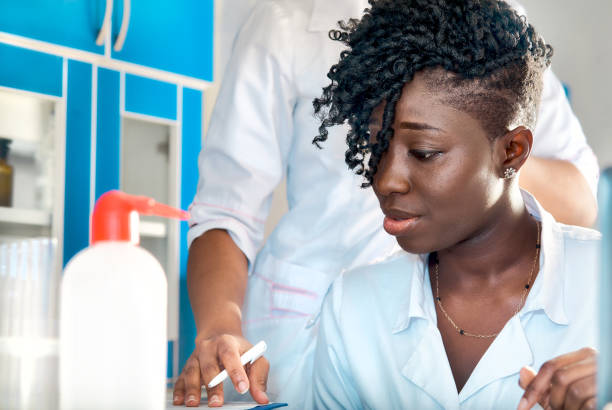 jeune médecin africain attrayant, infirmière ou étudiant en médecine avec des cheveux afro dans la robe blanche protectrice, écriture de travail de manteau dans le laboratoire de recherche, laboratoire d’essai ou société pharmaceutique pharmaceuti - biotechnology student laboratory nurse photos et images de collection