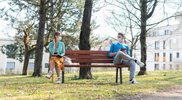 Woman and man with face mask in social distancing flirting Woman and man with face mask in social distancing flirting sitting on a park bench social distancing stock pictures, royalty-free photos & images