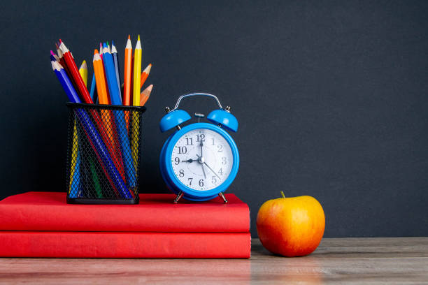 istock The blue alarm clock along with multi-colored pencils stand on a stack of red books, next to an apple 1214932161