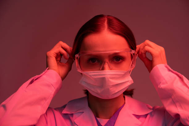 istock Virologist in protective eyeglasses and whitecoat putting mask on her face 1214933163
