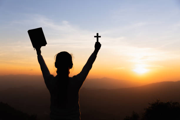 istock human hands praying to the GOD while holding a crucifix symbol with bright sunbeam. 1214936077