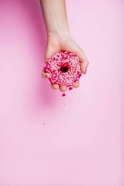 istock Woman Hand Smashing Donut on pink background 1214937063