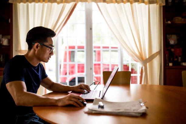 un hombre maduro chino de asia está trabajando en casa. escribir en la computadora, contento, propietario de una pequeña empresa - working at home mature adult small business laptop fotografías e imágenes de stock