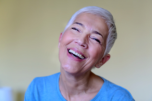Casual portrait of a beautiful mature woman with grey hair, looking at the camera and smiling confidently.