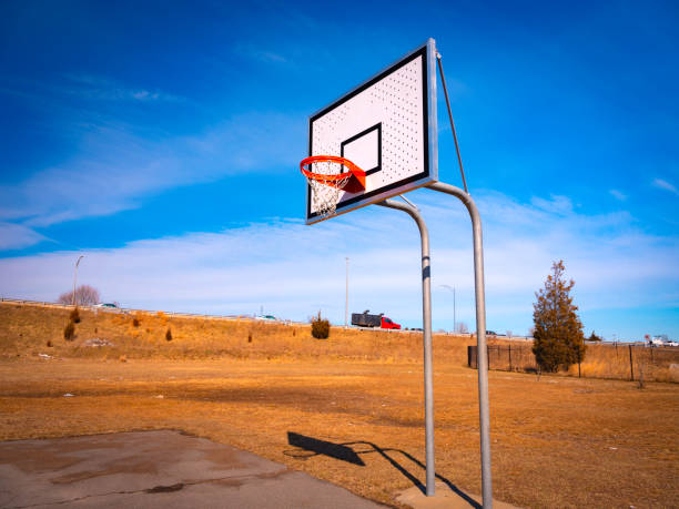 Partial basketball court with hoop on blue cloudy sky and grassy meadow backgrounds Basketball hoop on rest area neighborhood off-highway on a sunny day asphalt basketball court stock pictures, royalty-free photos & images