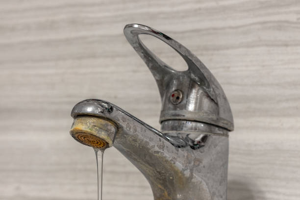 a thin stream of hard water flows from an old tap aerator. old bathroom sink faucet contaminated with calcium and grime. - harsh conditions imagens e fotografias de stock