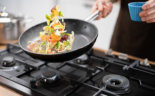 Unrecognizable chef throwing veggies and meet in the wok.