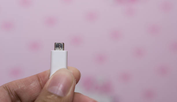 istock Hand holding micro USB cable for charging smartphone. Close Up man hand holding USB connector on pink background. 1214952380