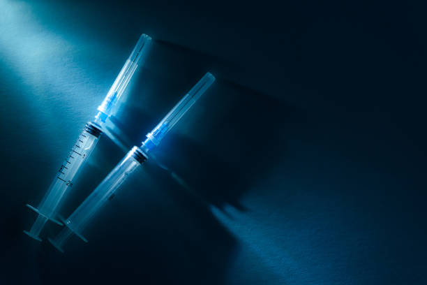 istock Two disposable syringes on a dark blue dramatic background. Vaccination and virus protection concept 1214952792