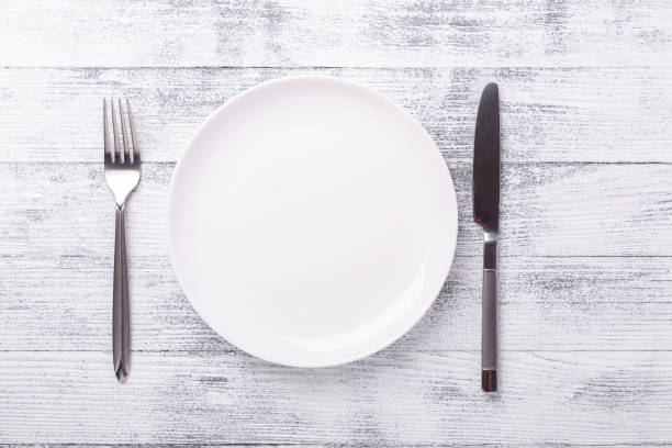 Empty white plate and cutlery on wooden background. Copy space. Top view stock photo