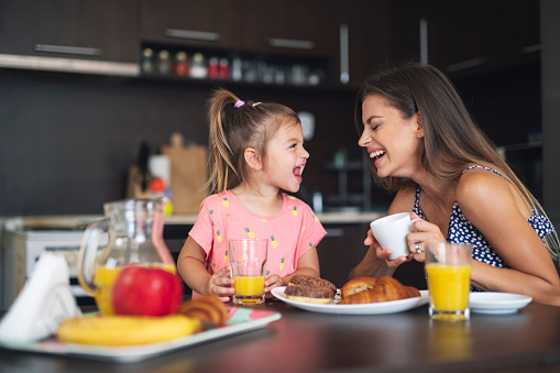 Mother and daughter having fun at breakfast in home, they smiling