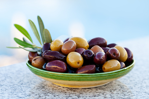 Assortment of fresh olives on a plate with olive tree leaves. Close up.