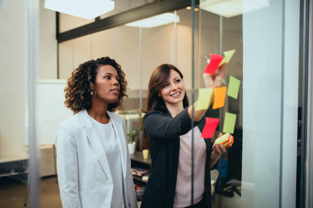 istock Two colleagues working together, sticking notes on glass wall in the office. 1214963131