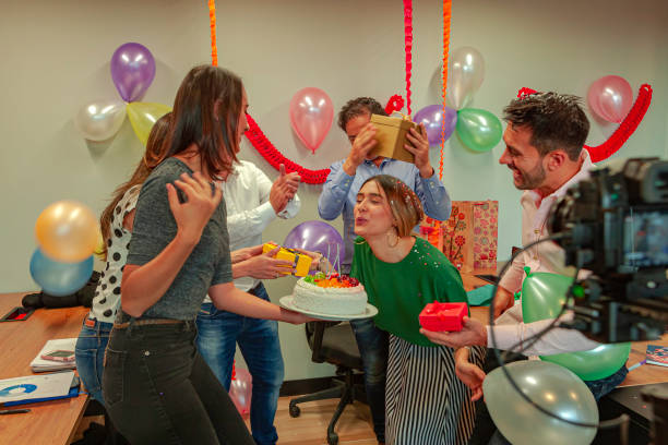 латиноамериканские белые воротнички празднуют день рождения молодой коллеги-женщины в их украшенном офисе. воздушные шары, конфетти, торт, - office fun group of people white collar worker стоковые фото и изображения