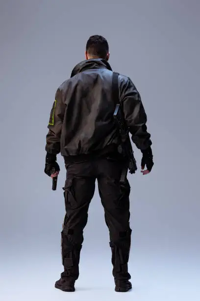 Photo of back view of cyberpunk player holding gun and standing on grey