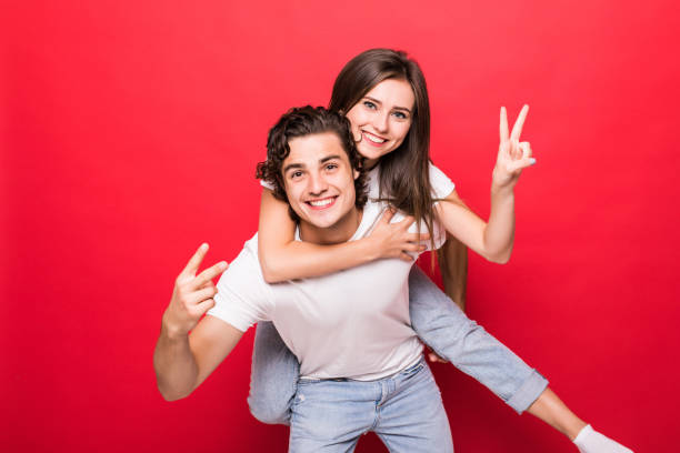 istock Handsome young man giving piggy back to his girlfriend on red background 1214965528