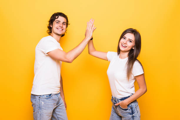 istock Friendly young people man and woman in basic clothing laughing and giving high five isolated over yellow background 1214966202