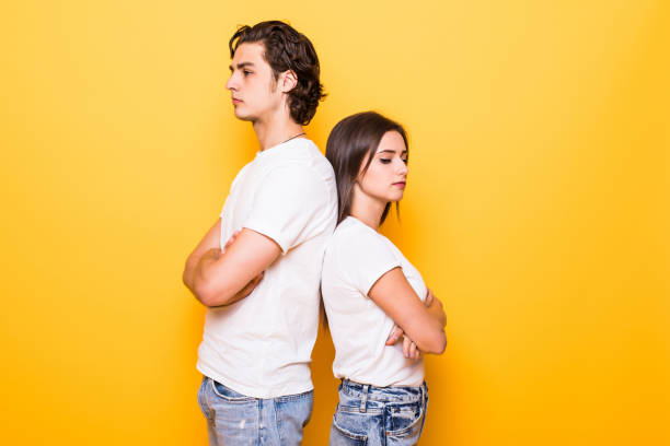 istock Confused young couple standing with one another's back and looking at the camera with crossed arms over yellow background 1214966413