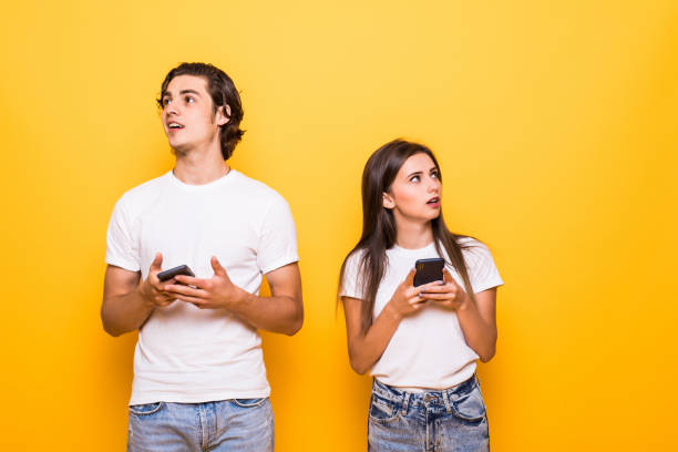istock Beautiful people man and woman smiling while both using mobile phones isolated over yellow background 1214966974