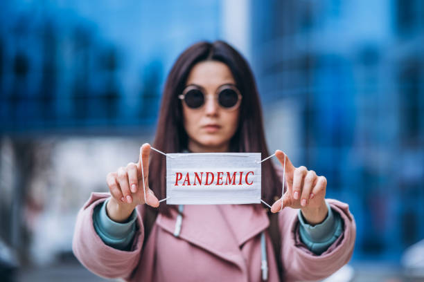 Female holding medical mask outdoors in the city with the pandemic inscription on it. Health protection and prevention of virus outbreak, coronavirus, COVID-19, epidemic, pandemic, infectious diseases, quarantine concept mujer sosteniendo máscara médica al aire libre en la ciudad con la inscripción pandémica en ella. protección de la salud y prevención del brote de virus, coronavirus, covid-19, epidemia, pandemia, enfermedades infecciosas, concepto de cuarentena.