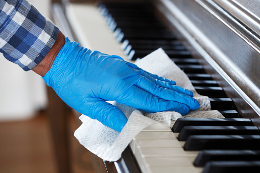 A close up of a man wearing a disposable glove cleaning piano keys with a disinfectant wipe.