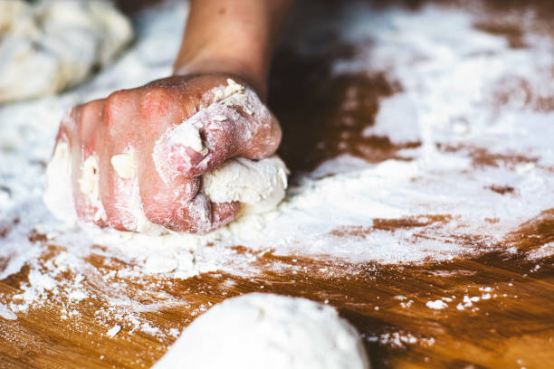 istock female hand kneading a flour dough by rolling it on a wooden board 1214970035