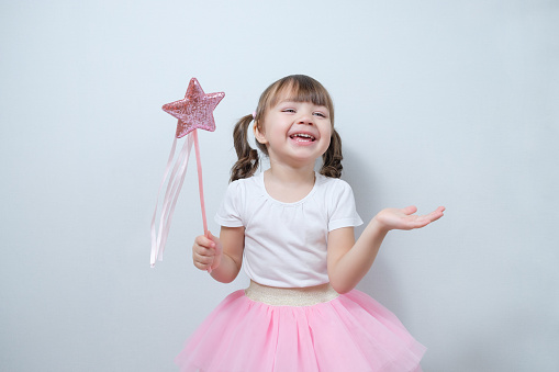 smiling little girl child holding a magic wand in his hand. A game of fairy, a sorceress. Performance of the play. Costume party