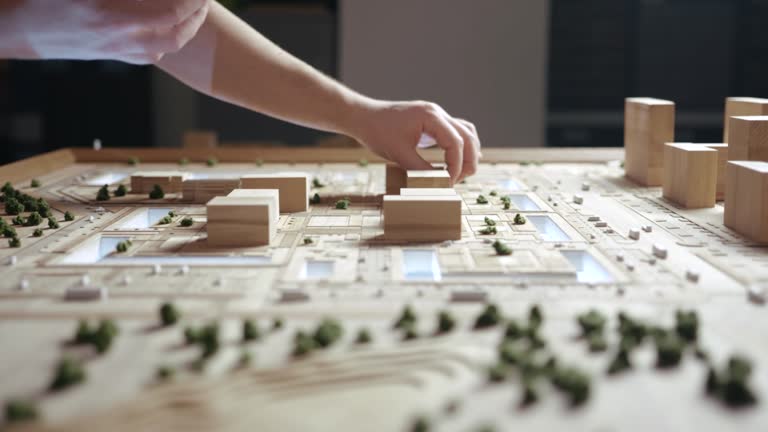 Person Decorates an Artificial Miniature Residential Quarter with Plants. Craftsman Arranges Decorative Shrubs with Fingers on a Wooden Layout. Caucasian Man Focused Addicting Hobby Close-up Shot