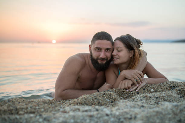 Romantic couple kissing on the beach. Young husband and wife in love together in the sand along the beach of mediterranean sea on sunst. Man hugging woman. Love is in the air.