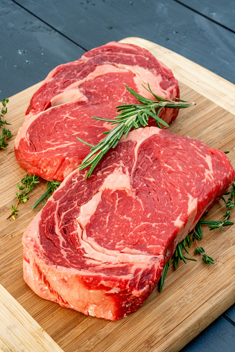 Raw Organic ribeye steaks with fresh herbs on a cutting board