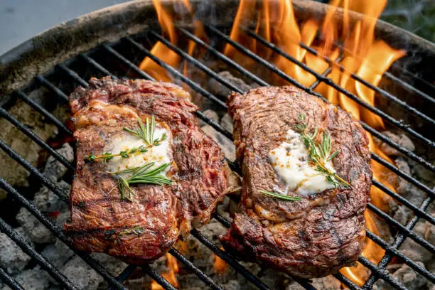 A fiery grill with two juicy ribeye steaks