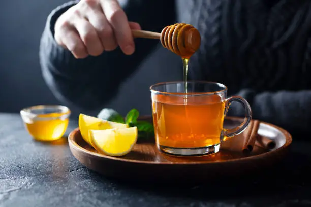 Photo of Cup of tea with pouring honey and lemon. Grey background.