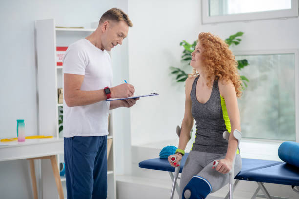 istock Male physiotherapist making notes, female patient sitting with crutches 1214979378