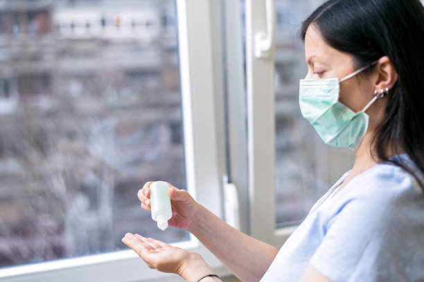 Young woman wearing protective medical mask while applying hand sanitizer stock photo