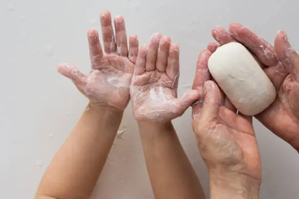 Photo of Top view of soaped child and woman hands holding soap on the white background