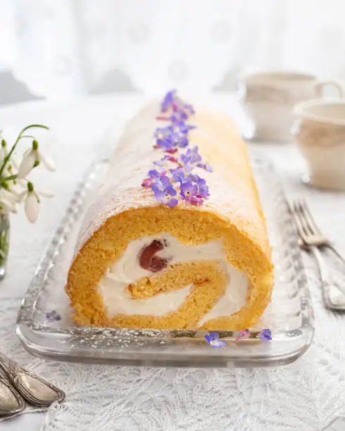 Swiss roll filled with whipped cream and strawberries, decorated with wild edible plants - veronica and purple dead-nettle