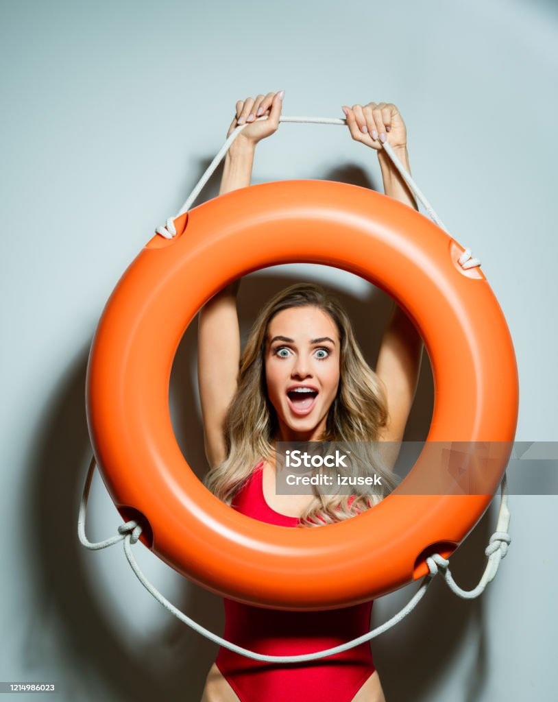 Summer portrait of excited woman holding life buoy Portrait of beautiful long hair young woman wearing red swimsuit, holding orange life buoy, laughing at camera. Studio shot on white background. Women Stock Photo