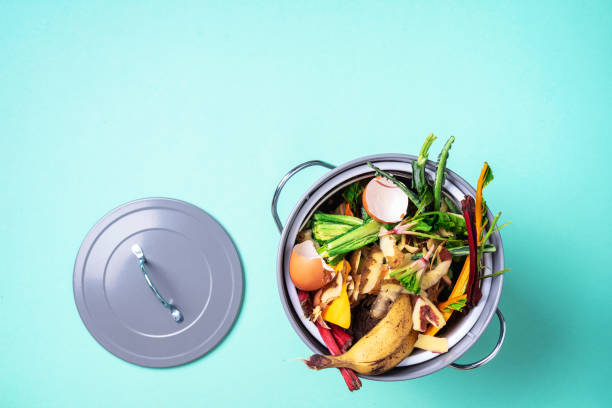 istock Peeled vegetables on chopping board, white compost bin on blue background. Top view of kitchen food waste collected in recycling compost pot. 1214986532