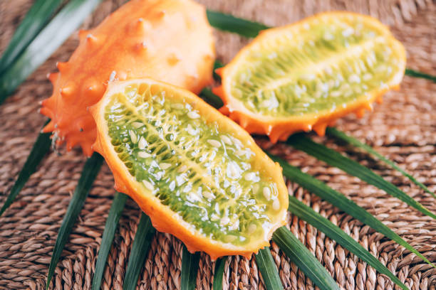 kiwano ou melon à cornes africaines avec des feuilles de palmier sur fond de rotin. gourde à haux coupée, concombre à cornes africaines, tomate anglaise. concept de fruit exotique - kawani fruit photos et images de collection